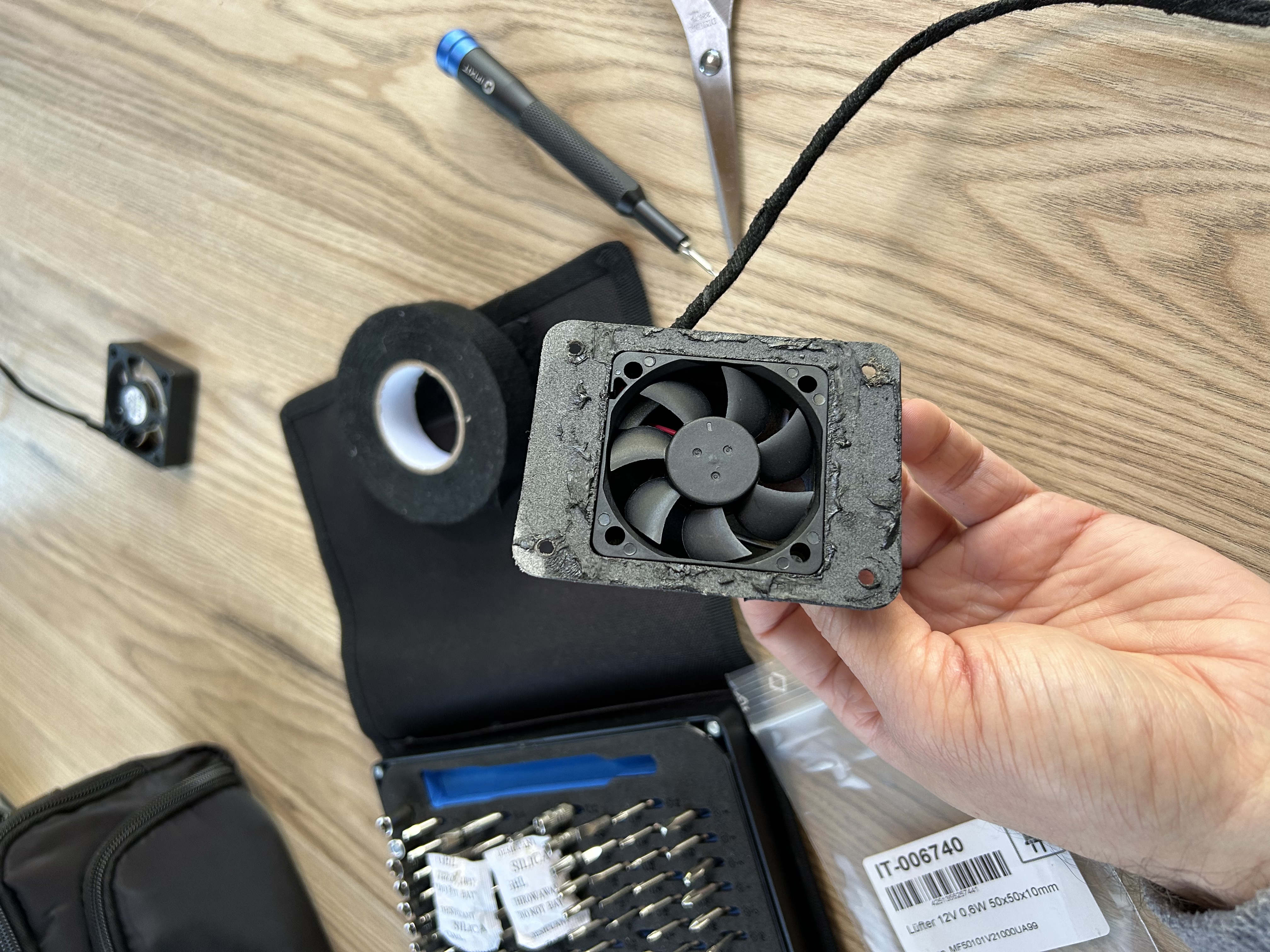 Zdjęcie rozebranej obudowy wentylatora toalety separacyjnej z resztkami taśmy butylowej. W tle stary wentylator, zestaw ifixit, nożyczki i taśma parciana.