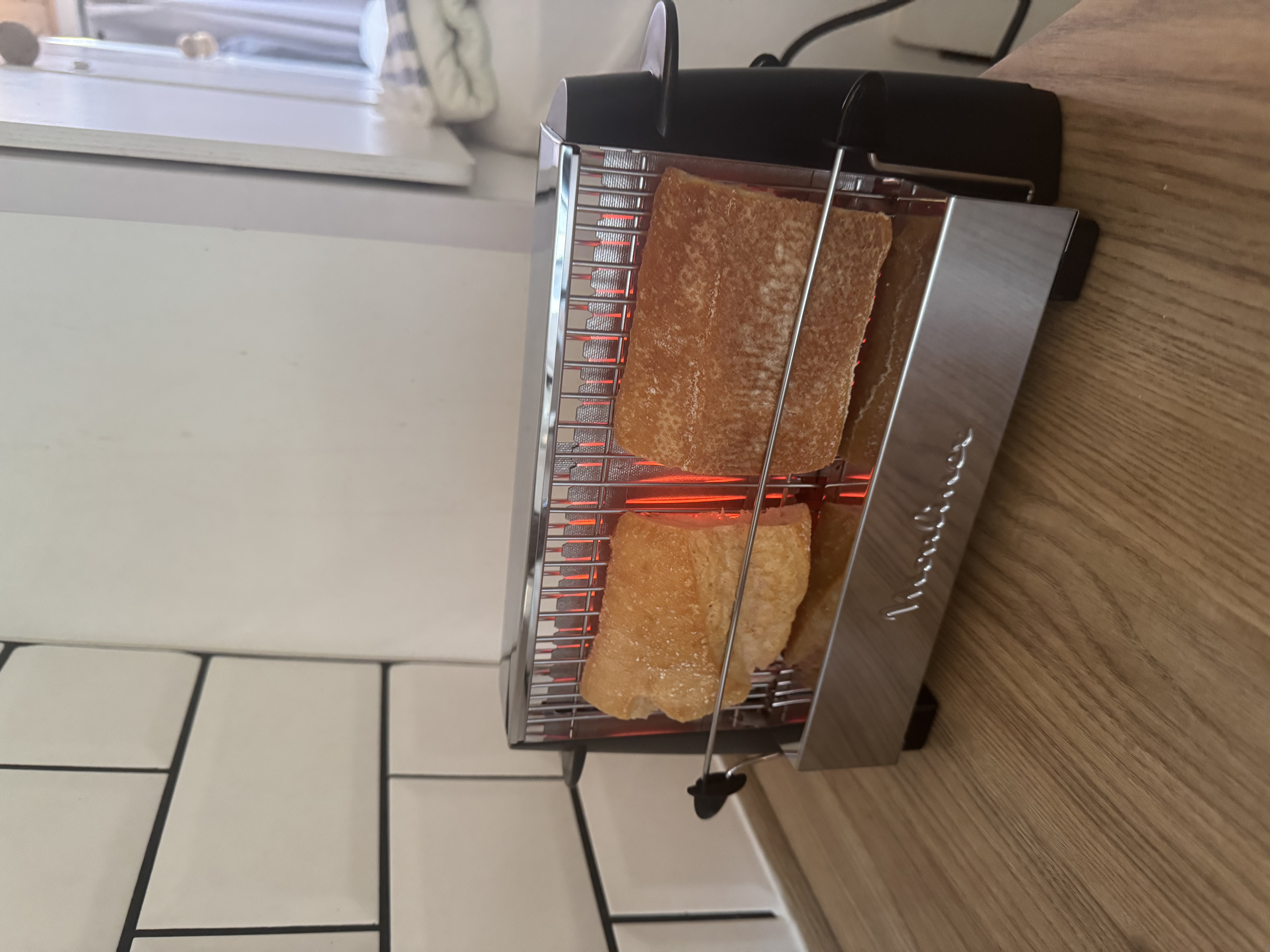 Zdjęcie tostera o otwartej konstrukcji opiekającego bagietkę.