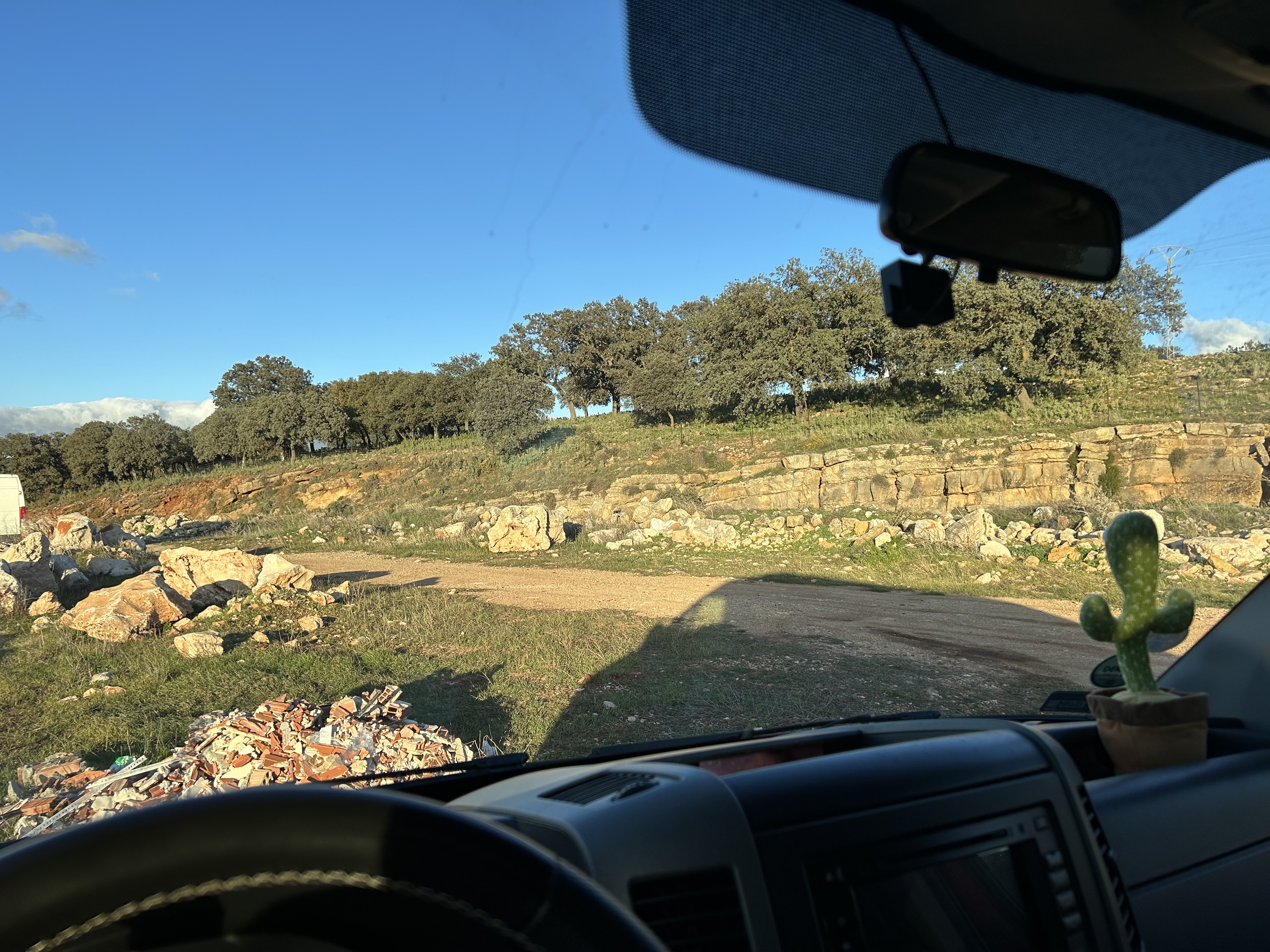 Zdjęcie widoki za przednia szyba kampera - tył białego vana, gruz i kawałek szutrowej drogi.